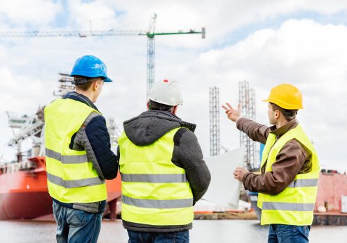 Senior engineer builder at the construction site in a port. Wearing safety helmet and yellow vest. Ship building industry.