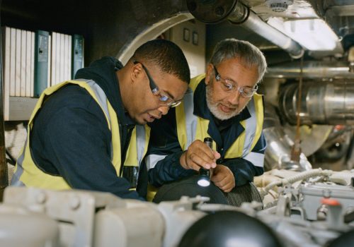 Mature engineers working to repair a machine with mechanical tools and equipment together. Professional industry workers doing quality control checks on systems. Skilled coworkers doing maintenance.